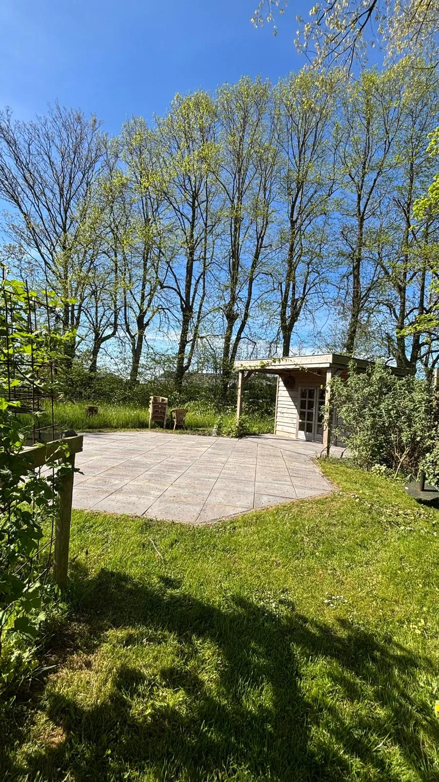 Het betegelde terras in de tuin met het tuinhuis onder de hoge bomen