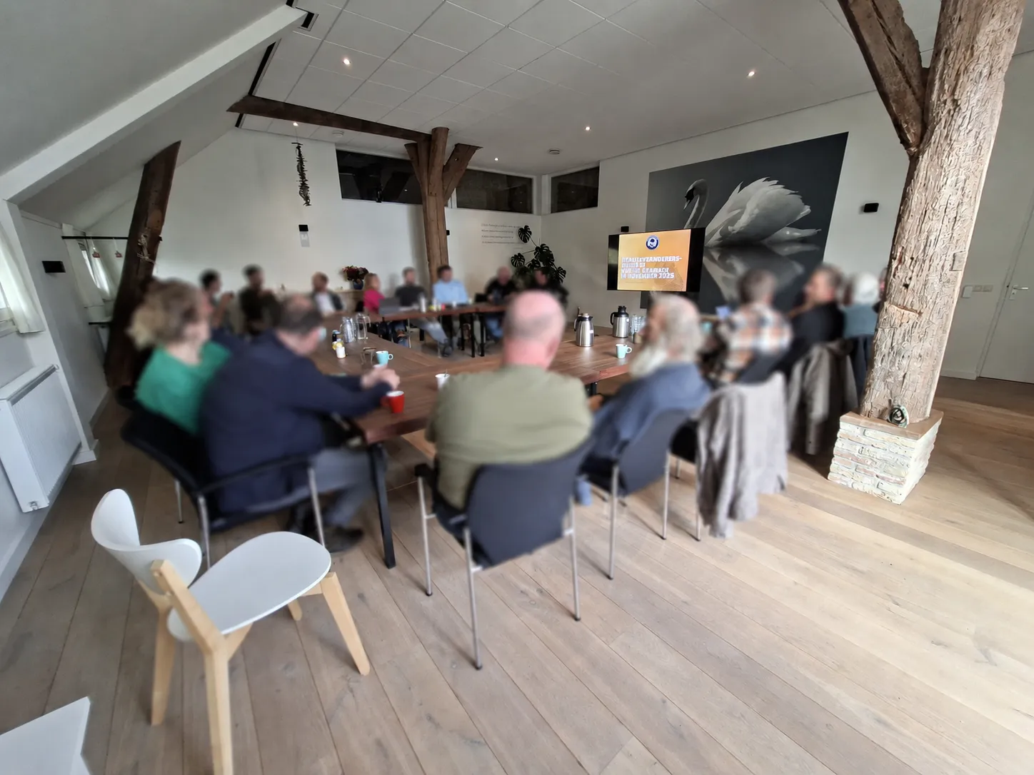 Een groep deelnemers aan tafel in de vergaderzaal, met het presentatiescherm aan